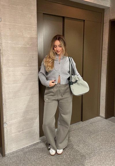 Suéter recortado de canalé gris claro, pantalones de chándal anchos verde oliva con cordón, zapatillas crema y un suave bolso de hombro gris.