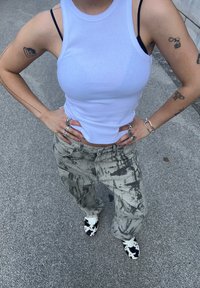 Top en débardeur blanc ajusté, pantalon large à motifs gris et chaussures en imprimé vache noir et blanc. Les accessoires incluent plusieurs bagues et bracelets.