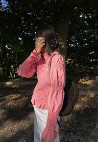Rot-weißes Gingham-Bluse mit Puffärmeln, gerafftem Design, kombiniert mit weißen Hosen und einer dunkelbraunen Schultertasche.