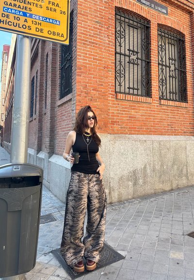 Pantalones anchos y estampados en tonos de beige y marrón con un diseño de rayas de tigre; combinados con una blusa negra ajustada y zapatos de plataforma.
