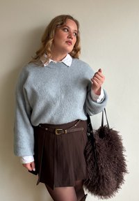 Hele sinine soonikkoes kampsun valge kraega särgi peal, harmoneerub pruuni volditud vööga seelikuga. Ühe käe peal ripub pehme, tumepruun kott.