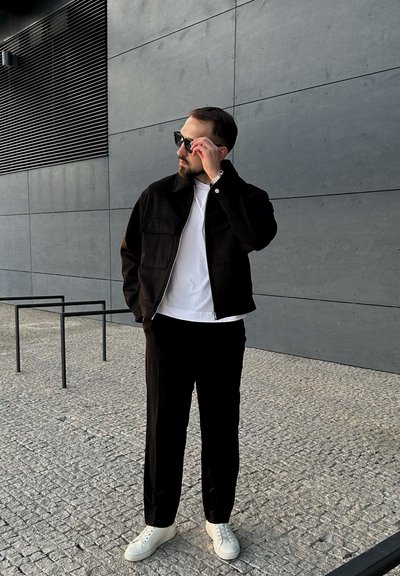 Chaqueta negra con cremallera frontal, camiseta blanca, pantalones negros y zapatillas blancas; textura suave y diseño a medida.