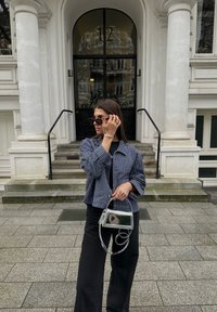 Pásikavý námorníkový sako, čierne široké nohavice a priehľadná kabelka so špirálovou rúčkou. Doplnky zahŕňajú nadmerné slnečné okuliare a náramky.