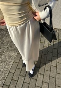 Kremowy body, jedwabna biała spódnica midi, czarna torebka oraz czarne buty z kokardą, wszystko na tle kamiennego chodnika.