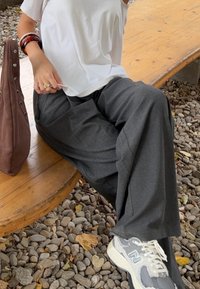 Pantalon large gris associé à une chemise blanche légère, complété par des baskets New Balance grises et un sac marron avec des accents argentés.