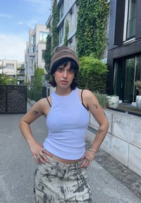 Débardeur blanc côtelé à fines bretelles associé à un pantalon taille haute à motif marbré gris. Porté avec un bonnet en tricot marron et noir.