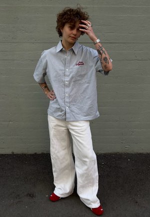 Gestreiftes Hemd in Hellblau und Weiß mit roter Stickerei, kombiniert mit weiten weißen Hosen und roten Socken, die einen lässigen Look zeigen.