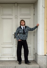 Pantalon noir à jambes larges associé à une veste boutonnée à motifs avec un col noir, portée sur une chemise blanche et une cravate noire.