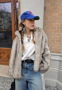 Grau gefütterte Jacke aus faux Fur, lässiger Schnitt mit strukturiertem Oberflächen; darunter ein weißer Zopfmuster-Pullover; blauer Baseballmütze mit Logo; hochtaillierte Jeans.