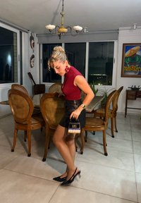 Svart mini kjol, åtsittande vinröd topp, svarta slingback klackar. Bär en liten handväska med svart och vävt mönster, i en modern matplats.