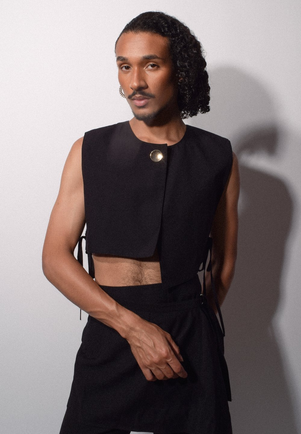 Svart kort topp med en rund guldknytnad. Har en strukturerad design och knyts på sidorna. Slät textur med minimalisk stil.