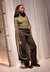 Oliwkowa bluzka z długim rękawem, prążkowana, z listwą na guziki, zestawiona z ciemnobrązowymi spodniami o prostych nogawkach. Dopełniona czarną torebką z złotym łańcuszkiem.