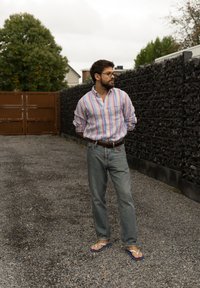 Cămașă cu dungi, blugi de culoare albastru deschis și sandale de plajă. Cămașa are culori pastelate, iar blugii sunt larghi și clasici.