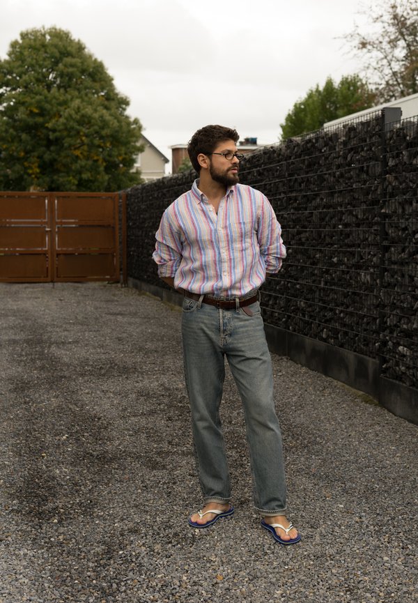 Gestreiftes Button-Up-Hemd, hellblaue Jeans und Flip-Flops. Das Hemd hat Pastellfarben, während die Jeans locker sitzend und klassisch sind.