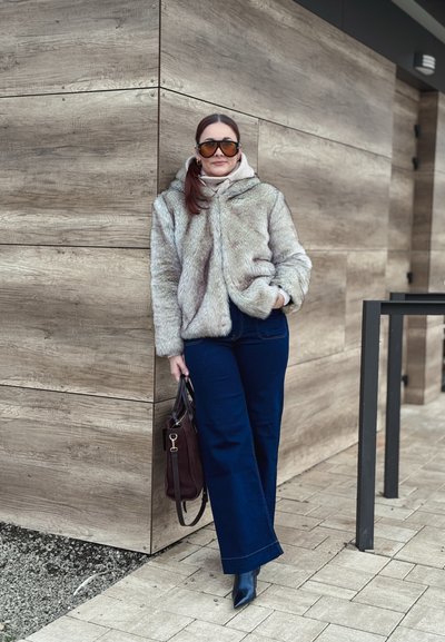 Chaqueta de piel sintética en gris claro, combinada con vaqueros de pierna ancha en azul oscuro. Botas negras de piel con punta afilada y un bolso oscuro con correa para el hombro.