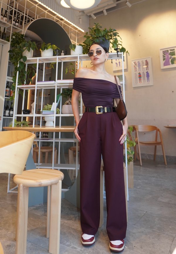 Burgunderfärgad off-shoulder topp i kombination med vida byxor, svart bälte och kraftiga sneakers. Solglasögon och minimala accessoarer fulländar looken.