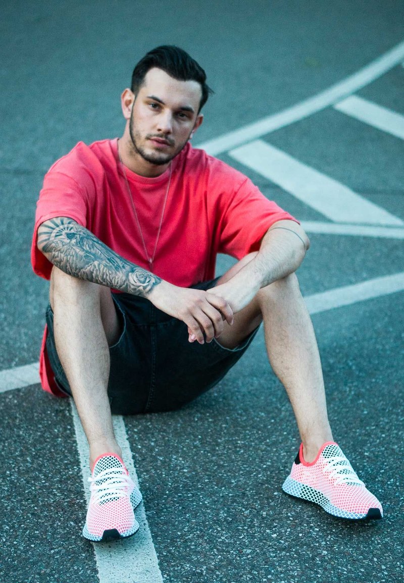 Strick-Sneaker in einer weißen und rosa Farbgestaltung, mit Mesh-Material, schwarzen Akzenten und einer strukturierten Sohle, auf einer gepflasterten Oberfläche platziert.