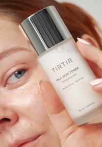 Przezroczysta szklana butelka z srebrną nakrętką, oznaczona napisem "TIRTIR MILK SKIN TONER". Pojemność 50 ml. Gładka tekstura, widoczna biała ciecz w środku.