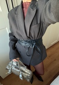 Blazer gris surdimensionné avec une ceinture en cuir noir, accompagné d'un sac à main argenté scintillant en sequins et de chaussures pointues noires.