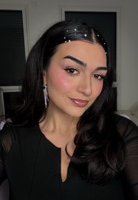 Black top with a V-neck, sheer sleeves. Long, curly dark hair with silver rhinestones. Statement crystal earrings hang from the ears.