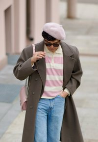 Lang brun frakk, lys rosa beret, stripete genser (rosa og hvit), lys blå jeans og en rosa håndveske med kjede.