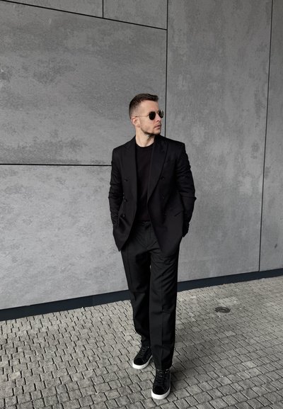 Blazer negro de doble botonadura sobre una camiseta negra, combinado con pantalones negros. Completan el look unas zapatillas negras con detalles blancos.