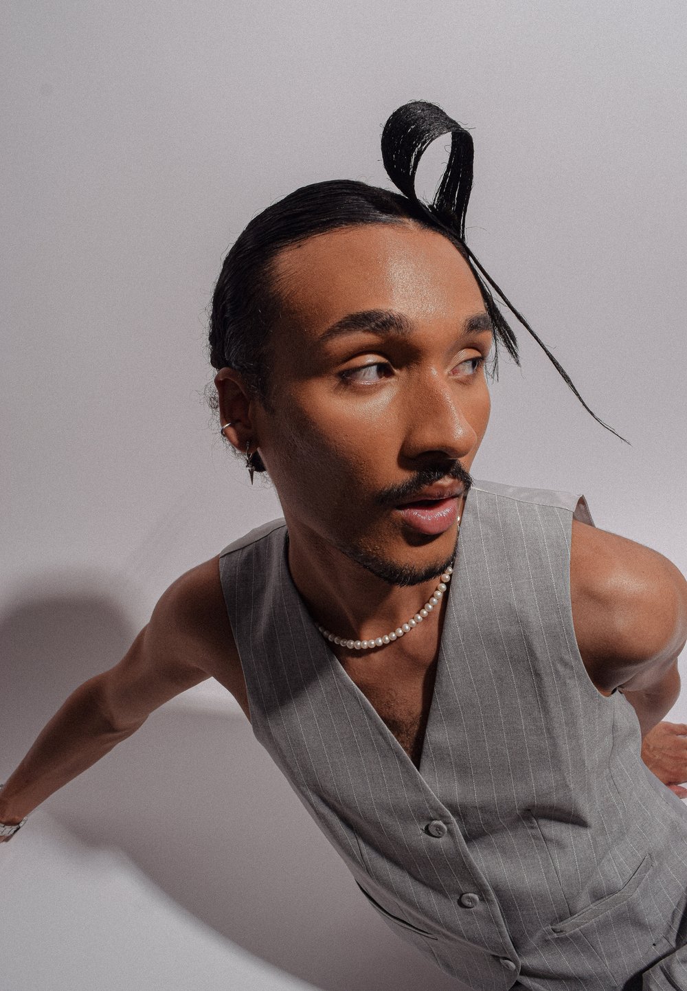 Gilet gris à rayures avec deux boutons, assorti à un collier de perles. Cheveux coiffés en une longue forme tordue. Peau au texture lisse.