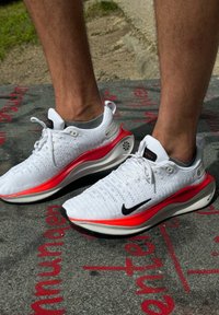 Valged spordijalatsid punaste aktsentidega, tekstureeritud pealis, must Nike'i logo ja polsterdatud põhi. Omab ümmargust auku paelte jaoks.
