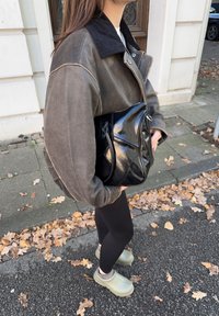 Brun och svart tvåfärgad jacka med manchesterrygg, svart väska, svarta leggings och olivfärgade träskor på en trottoar med fallna löv.