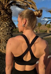 Brassière de sport noire avec bretelles croisées, matériau texturé et détail découpé au dos, portée avec les cheveux coiffés en chignon.