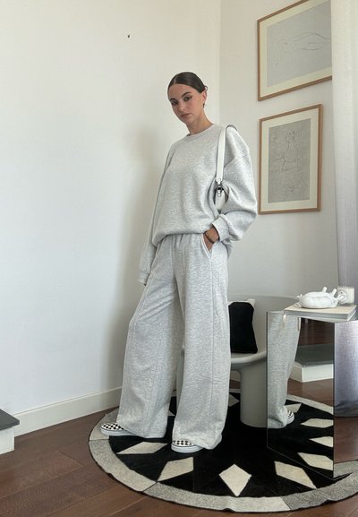 Sudadera gris claro y pantalones de pierna ancha hechos de un material suave similar al jerga. El conjunto se complementa con zapatillas de cuadros en blanco y negro.