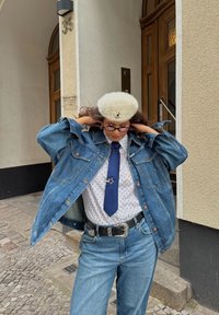 Denim jope, millel on kulunud detailid, polka punktidega särk, sinine lips ja valge barett. Pruunid juuksed, prillid ja must vöö hõbedaste aksessuaaridega.