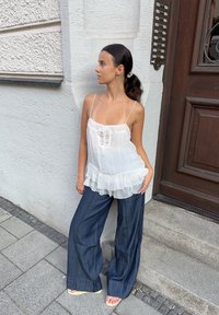 Balta, permatoma kamšytė su raukšlėmis apatinėje dalyje, derinama su laisvomis, tamsiomis džinsinėmis kelnėmis. Paprasti papuošalai ir švelni šukuosena užbaigia įvaizdį.