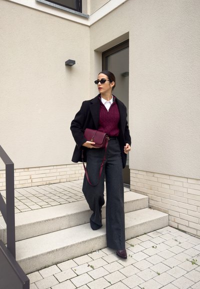 Pantalones de pierna ancha gris de mezcla de lana, suéter burdeos de punto trenzado, abrigo negro de doble botonadura y un bolso cruzado burdeos accessorios con gafas de sol.
