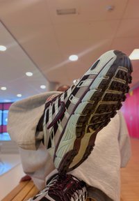 Scarpa da corsa con una combinazione di colori nera, bianca e bordeaux. Presenta una suola testurizzata e una tomaia in rete con dettagli rossi e un sistema di allacciatura.