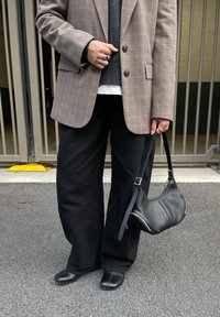 Brūns rūtainais žakete uz pelēka džempera fona, kombinēts ar melnām platām biksēm un melnu ādas plecu somu ar rāvējslēdzēja detaļām.