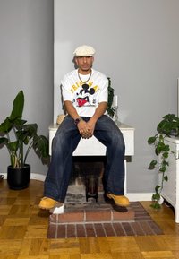 Valkoinen graafinen t-paita, jossa on musta ja punainen Mikki Hiiri -kuvio, yhdistettynä väljihin sinisiin farkkuihin ja keltaisiin työkenkiin.