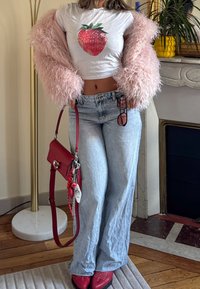 White cropped T-shirt with a strawberry graphic, pink fuzzy jacket, light blue wide-leg jeans, red handbag, and coordinating shoes.