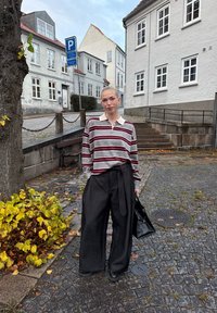 Szaro-bordowa w paski, długorękawowa koszulka polo, zestawiona z czarnymi, wysokim stanem, szerokimi spodniami, trzymając czarną torbę na ramię.