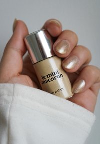 Gold nail polish bottle with silver cap; features brand name "le mini macaron." Hand displaying shiny gold nails, holding a white sleeve.