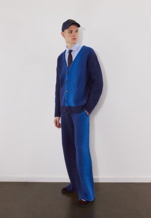 Cardigan in a blue gradient with buttons, teamed with coordinating wide-leg trousers. The fabric looks soft and fuzzy. Dark shoes round off the ensemble.