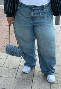 Calças de ganga oversized de cor azul claro com cintura alta, combinadas com uma pequena bolsa azul acolchoada e sapatilhas brancas.