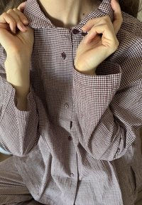 Kostium w kratkę w kolorze bordowym, z kołnierzykiem w kształcie stożka, długimi rękawami i luźnym krojem. Posiada ciemne guziki oraz teksturowaną tkaninę.