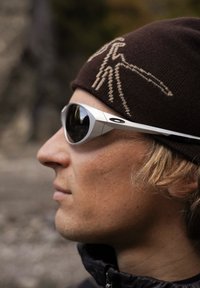 Sluneční brýle se stříbrným rámem a tmavými skly, které nosí osoba, spolu s hnědou pletenou čepicí se světlým vzorem.