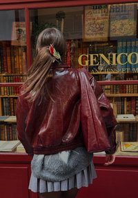 Bordo spalvos odinė bombonešio striukė su per didelėmis rankovėmis, pasiūta su ribuotu apačia, derinama su šviesiai pilku klostuotu sijonu ir gėlių plaukų segtuku.