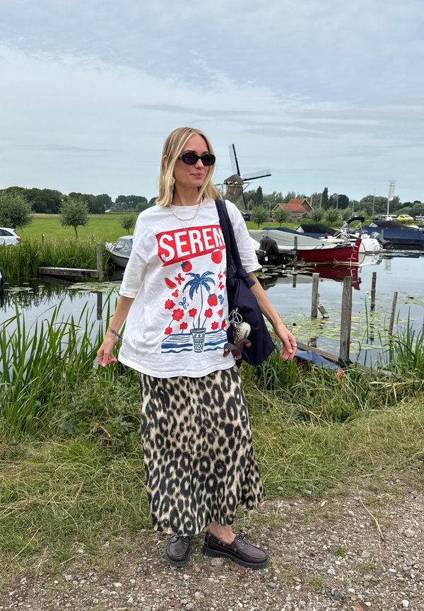Camiseta blanca de gran tamaño con diseño gráfico rojo, combinada con una falda maxi de estampado de leopardo. Los accesorios incluyen gafas de sol y un bolso de hombro.