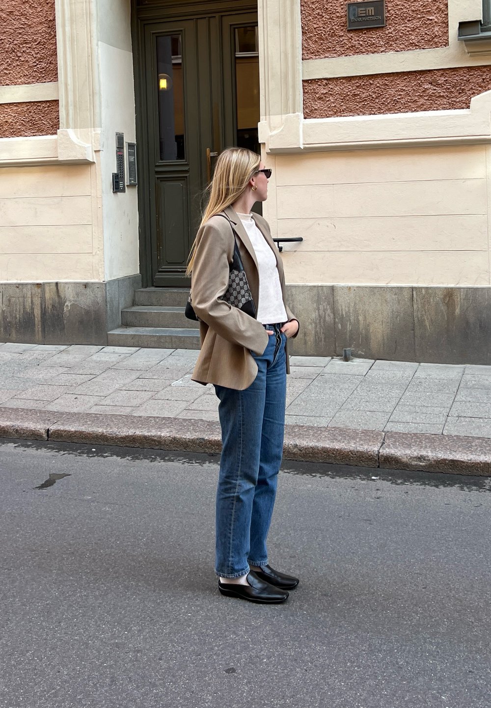 Καφέ σακάκι, λευκή μπλούζα, μπλε τζιν και μαύρη παπούτσια. Το σακάκι έχει κομψή γραμμή, ενώ η τσάντα διαθέτει ξεχωριστό σχέδιο.