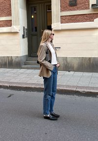 Καφέ σακάκι, λευκή μπλούζα, μπλε τζιν και μαύρη παπούτσια. Το σακάκι έχει κομψή γραμμή, ενώ η τσάντα διαθέτει ξεχωριστό σχέδιο.