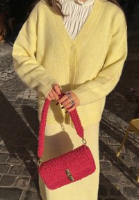 Cardigã amarelo de malha com decote em V, combinado com uma mala vermelha texturada com uma alça felpuda e detalhes em metal dourado.