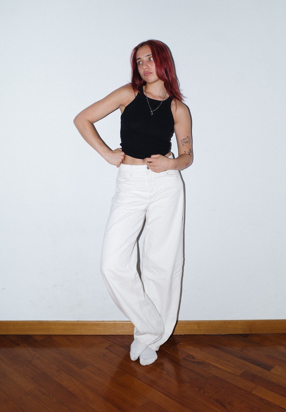 Czarny bezrękawnik crop top i białe spodnie z wysokim stanem i szerokimi nogawkami. Modelka stoi na tle gładkiej ściany, prezentując casualowy, nowoczesny strój.